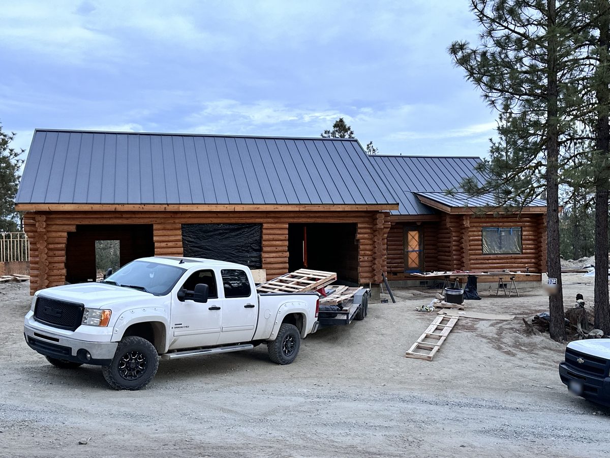 Front of the log home under construction with a white pickup truck