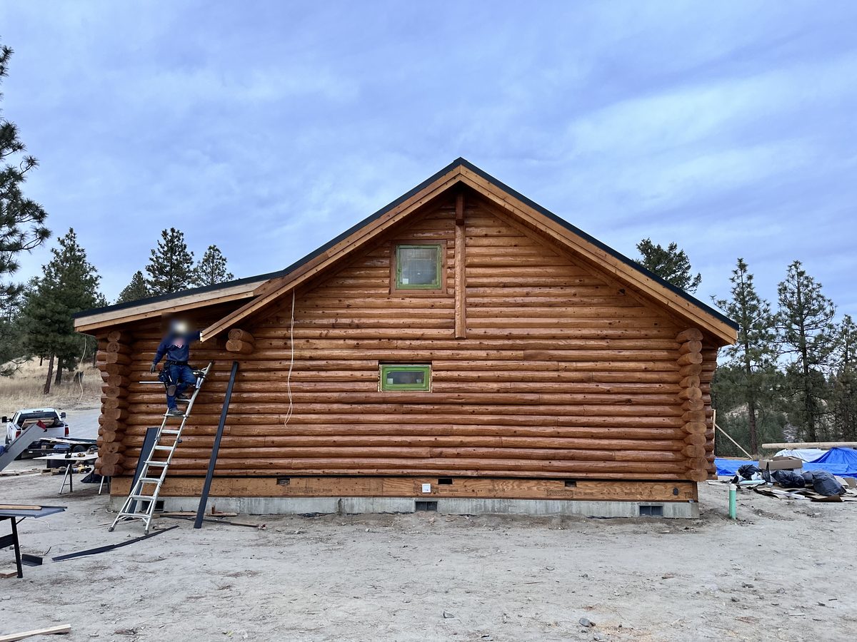 A worker on a ladder at the gable end of the log home